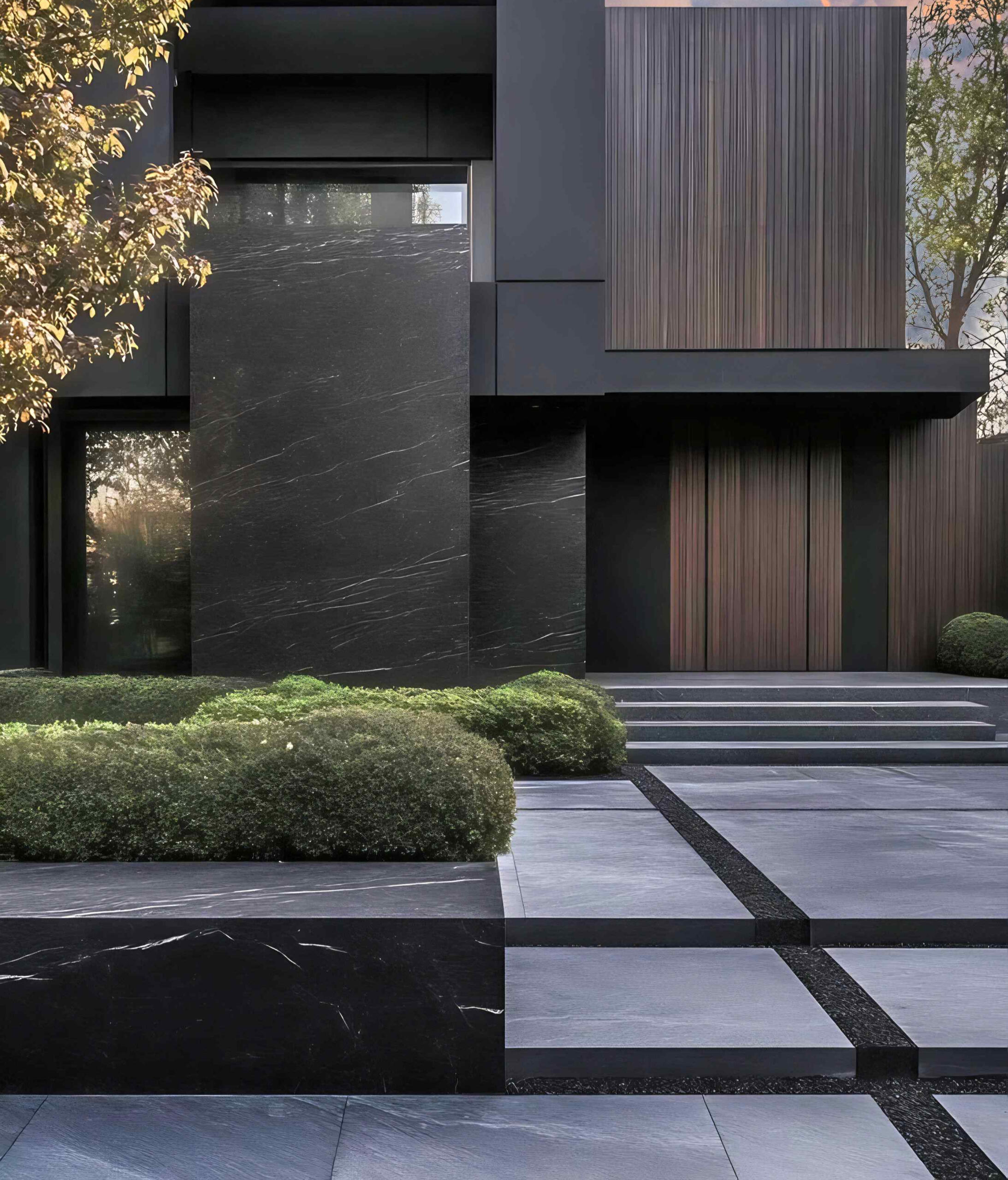 A modern home exterior featuring dark stone cladding, large-format stone slabs, and sleek architectural design with a landscaped entrance, created by Erb Rose Architectural.